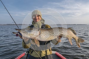 Pike fishing. Happy fisherman holding big fish at boat