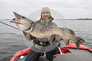 Pike fishing. Happy fisherman holding big fish at boat