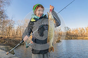 Pike fishing. Lady fisherwoman holding fish and tackle in hands