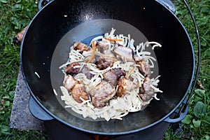 Pilaf. Cooking step by step. Step 3. Cooking meat wih onion in a cauldron. Pork is fried in oil over a fire.