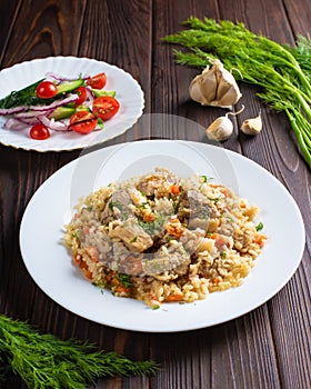 Pilaf with meat and salad in white plates on a wooden table.