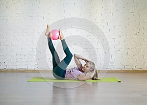 Pilates abs exercise with small fit ball. Caucasian woman doing workout in fitness studio.
