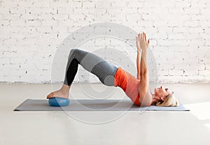 Pilates with small fit ball. Caucasian woman practice gluteal bridge balance on a mat, in loft white studio indoor