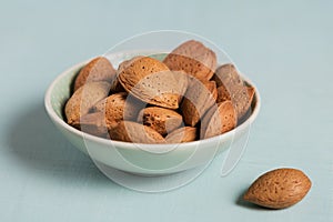 Pile of Almond nuts in a bowl on a light blue background