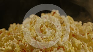 Pile of appetizing popcorn with dissipating steam. Unrecognizable person throws freshly cooked hot popcorn. Close up
