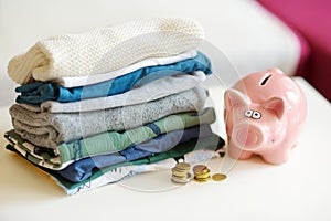 A pile of baby clothes, coins and a piggy bank. Parenting expenses concept. Working out a baby budget. Saving money when planning