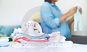 Pile of baby clothes, stuff and pregnant woman in home interior