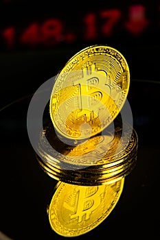 Pile of bitcoins with decreasing stock chart on mirrored reflective surface