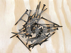 A pile of black self tapping screws on wooden.