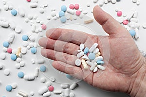 Pile of blue, white, pink and yellow colored pills and capsules with male hand