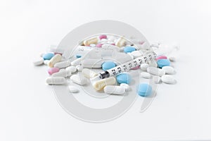 Pile of blue, white, pink and yellow colored pills and capsules with medical syringe