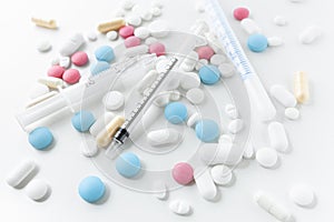 Pile of blue, white, pink and yellow colored pills and capsules with medical syringes