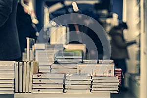 Pile of books, abstract blurred background in book store or in library. Unrecognizable people, bookshelves with books