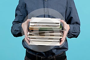 A pile of books in the hands of a teenager, among whom is a tablet