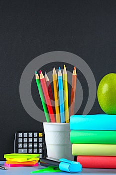 A pile books and stationery on a chalkboard background. Work desk, education, school