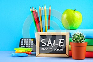 A pile of books and stationery on a chalkboard background. Work desk, education, school. SALE.