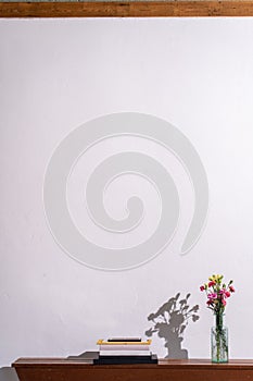 Pile of books and a vase with flowers on a wooden shelf against a white wall