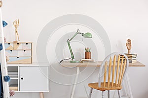 Pile of books, wooden hand and industrial mint colored lamp on stylish wooden desk in white kid`s bedroom