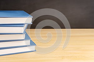 Pile of books on wooden table and black chalkboard at background with copy space