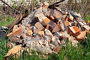 A pile of bricks from a demolished brick wall. A pile of broken bricks in the yard on the grass. pollution of nature by constructi