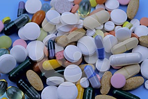 A pile of bright colored pills and capsules of medicines on a blue background.