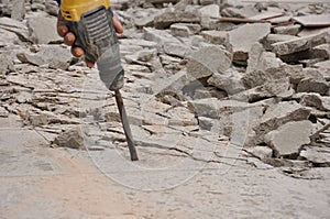 Pile of broken concrete, worker smashes concrete floor with electric hammer drill