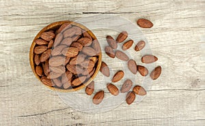 A pile brown seeds of Almond nut in wooden bowl and spill off on wooden table, top view angle of shooting with copy space