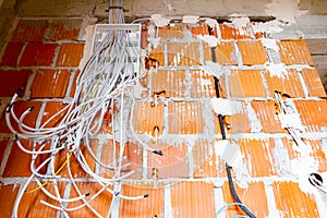 Pile of cables is hanging from a fuse box placed on the wall of unfinished building