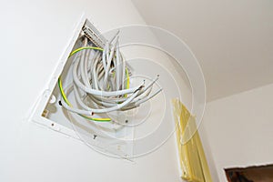 Pile of cables is hanging from a fuse box placed on the wall of unfinished building