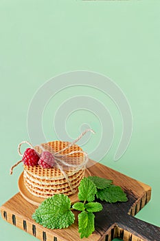 Pile of caramel round Dutch waffles with raspberries and melissa leaves on cutting board and blue background with copy space