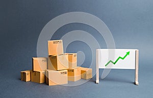 A pile of cardboard boxes and stand with green up arrow. Price increase. The growth rate of production. Increasing consumer demand
