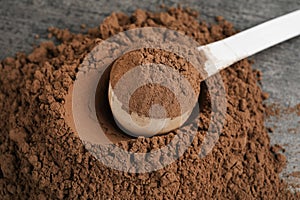 Pile of chocolate protein powder and scoop on grey , closeup