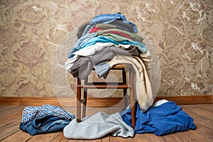 A pile of clothes is lying on a chair and on the floor. The concept of overconsumption and shopaholism photo