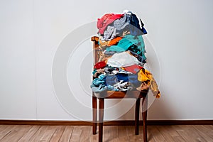 A pile of clothes stacked on a chair near the wall. The concept of overconsumption photo