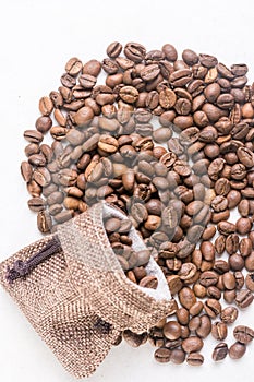 Pile of coffee beans and jute drawstring bag on the white background