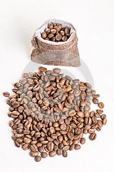 Pile of coffee beans and jute drawstring bag on the white background