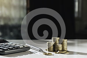 Pile of coins with a calculator and a pen on the table in finance concept