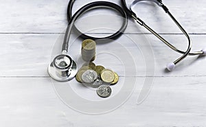 A pile of coins lies on the table and a stethoscope