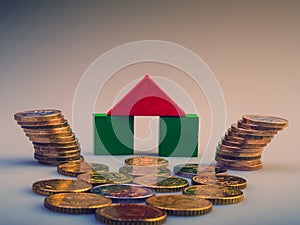 pile of coins and a model of a house on a light background. Business metaphor.