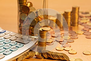 Pile of coins on a table with a lot of different coins around it and a calculator on a wooden table. Save money concept banner