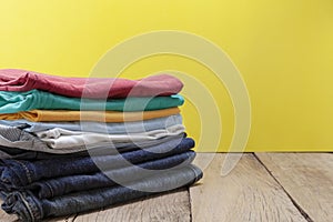 Pile of colored clothes on wood table yellow background