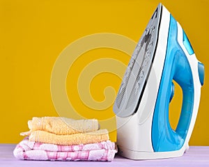 Pile of colorful clothes and irons, on pastel wooden plank ,yellow color background.