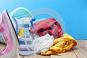 Pile of colorful clothes and irons,spray bottle on wooden plank ,blue color background