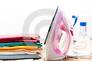 Pile of colorful clothes and irons spray bottle on wooden plank isolated on white background