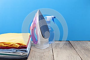 Pile of colorful clothes and irons,spray bottles,on wooden plank ,blue color background