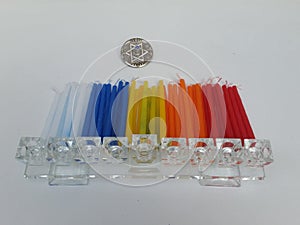 A pile of colorful Hannukah candles with a glass chanukkah lamp in the front and a dreidel in the back