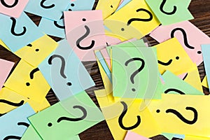 Pile of colorful paper notes with question marks on wooden background. Closeup