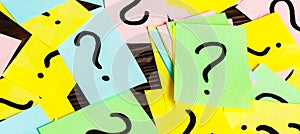 Pile of colorful paper notes with question marks on wooden background. Closeup