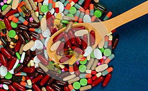 Pile of colorful tablets and capsules pills and wood spoon on blue background. Antibiotic resistance concept. Pharmaceutical