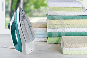 Pile of colorful towels and electric iron, ironing clothes concept